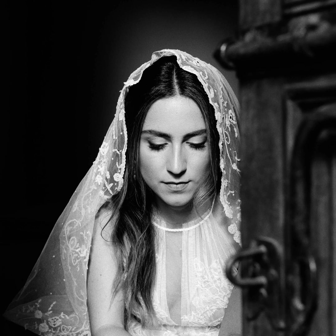 Black and white photo of Mariana in a lace veil and wedding dress, eyes closed in contemplation.