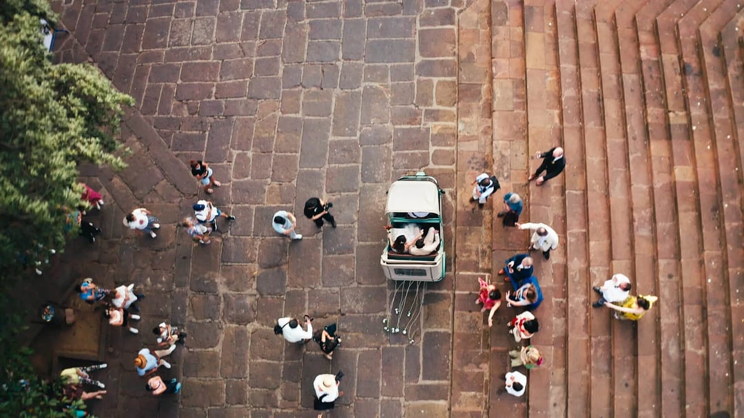 Overhead view of a wedding with a bride and groom in a carriage surrounded by guests.