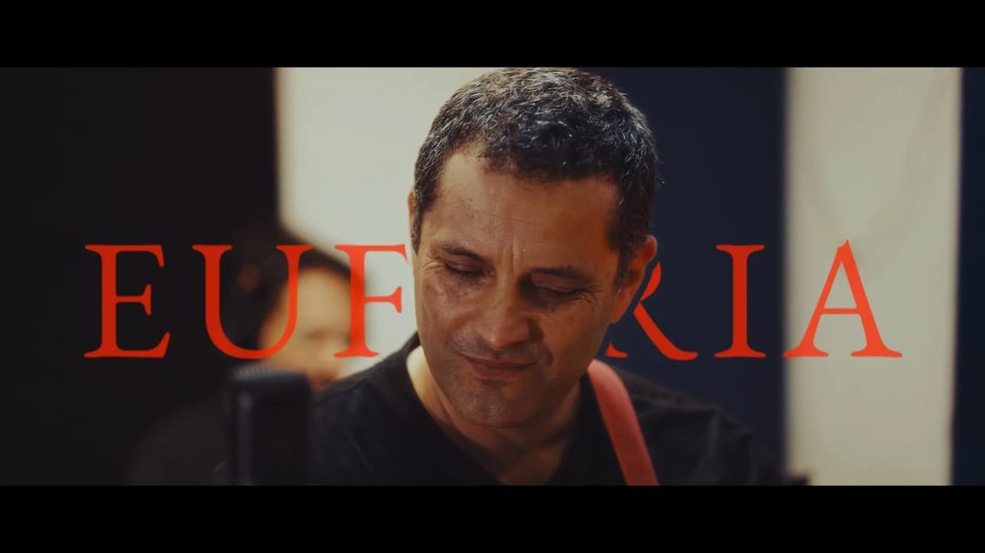 A musician looks down mid-performance in the studio, with the title Euforia set in red across the frame.