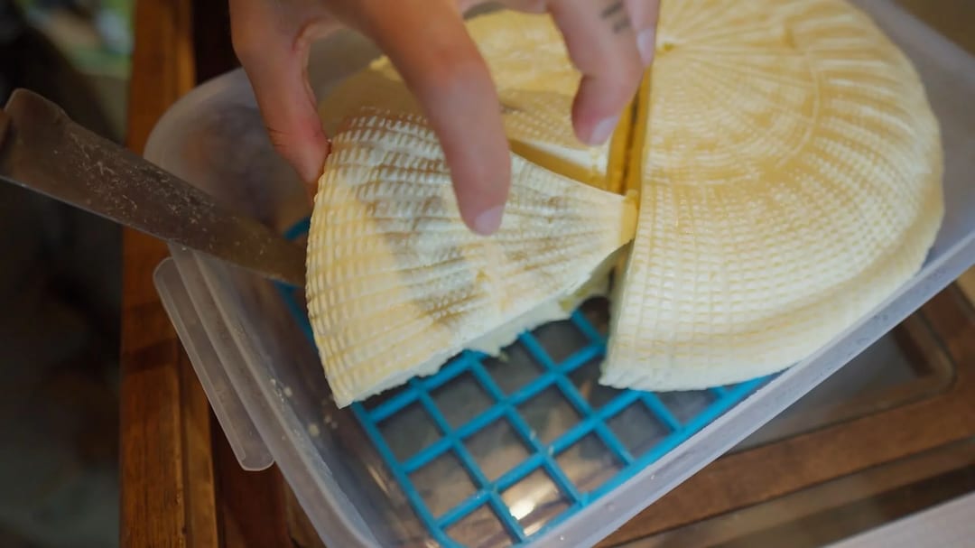 Rueda de queso artesanal cortada dentro de un recipiente.