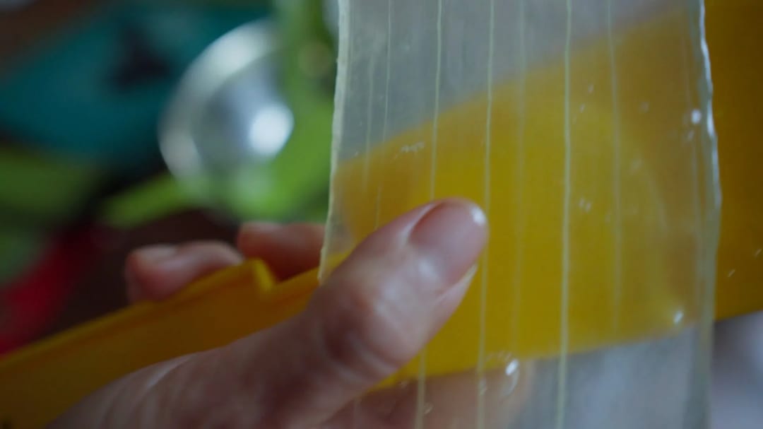Primer plano de una mano que sostiene un xilófono de juguete amarillo con sus cuerdas visibles.