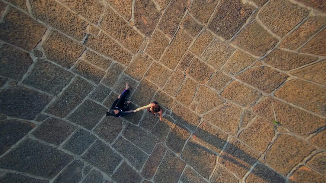 Aerial view of Cata and Carmen holding hands on a stone-paved surface.