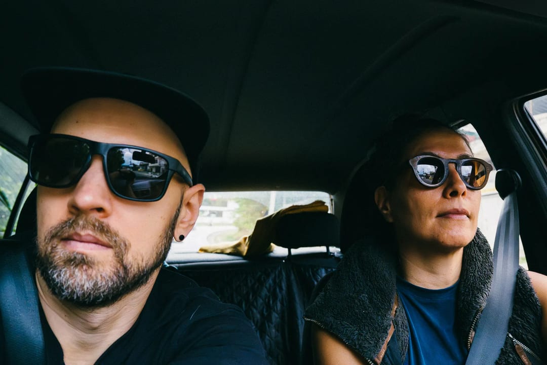 Couple in car wearing sunglasses and seatbelts, possibly traveling to El Páramo.