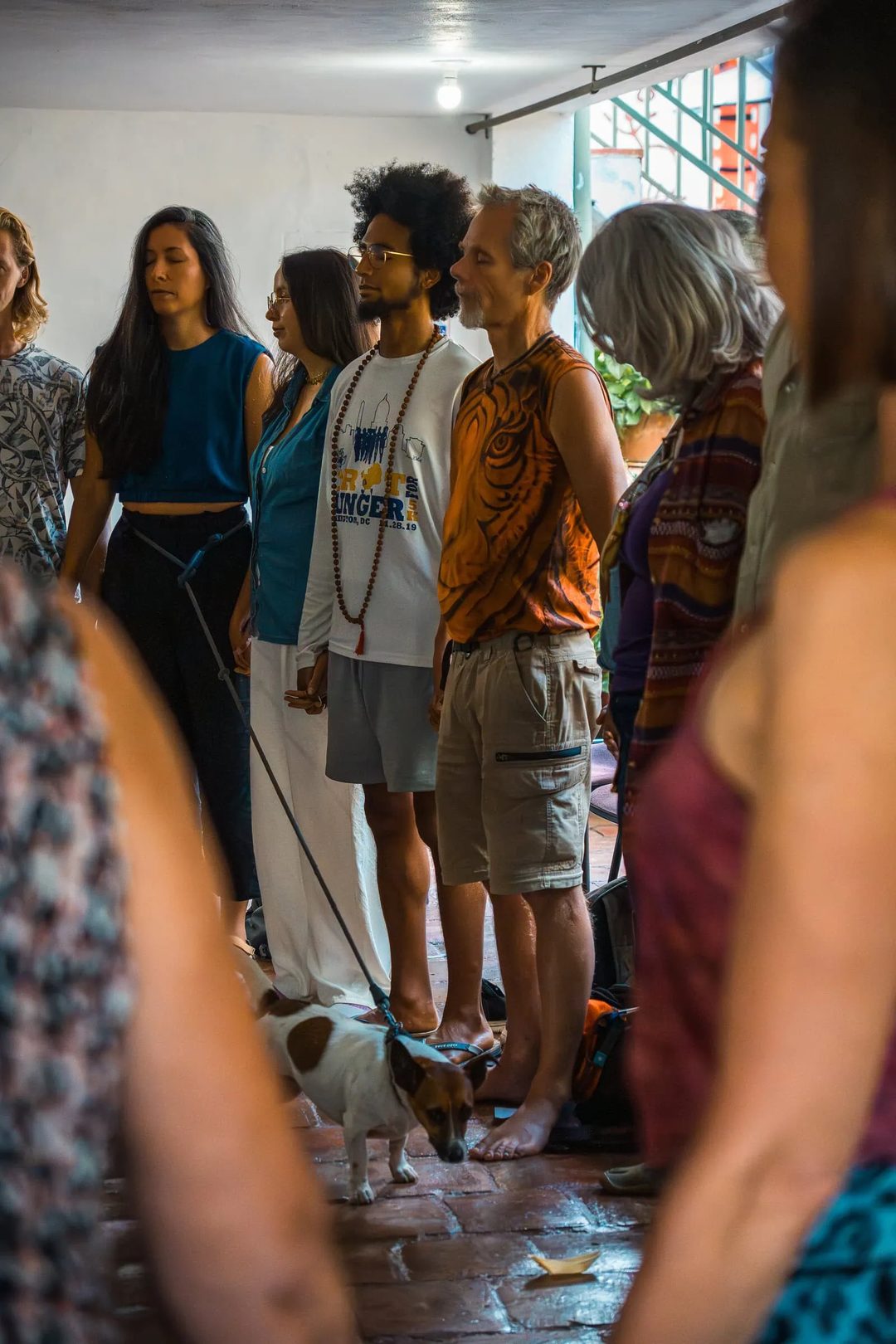 Participants stand in a circle with their eyes closed during an indoor group activity.
