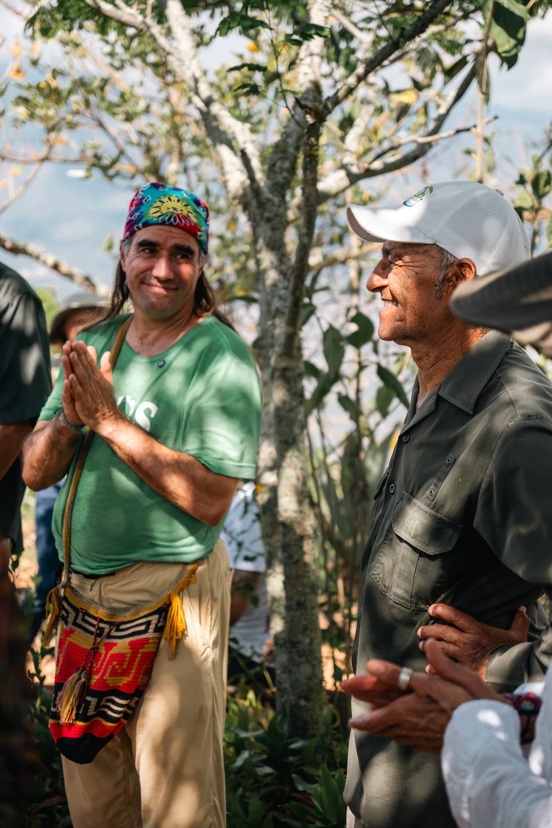Two men talk among trees during a Design School for Regenerating Earth field visit.