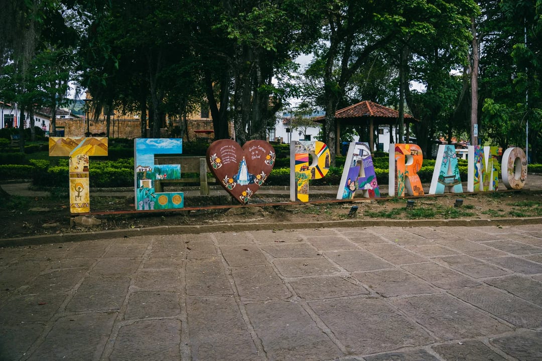 Colorful "El Páramo" sign in park, trees and buildings in background.