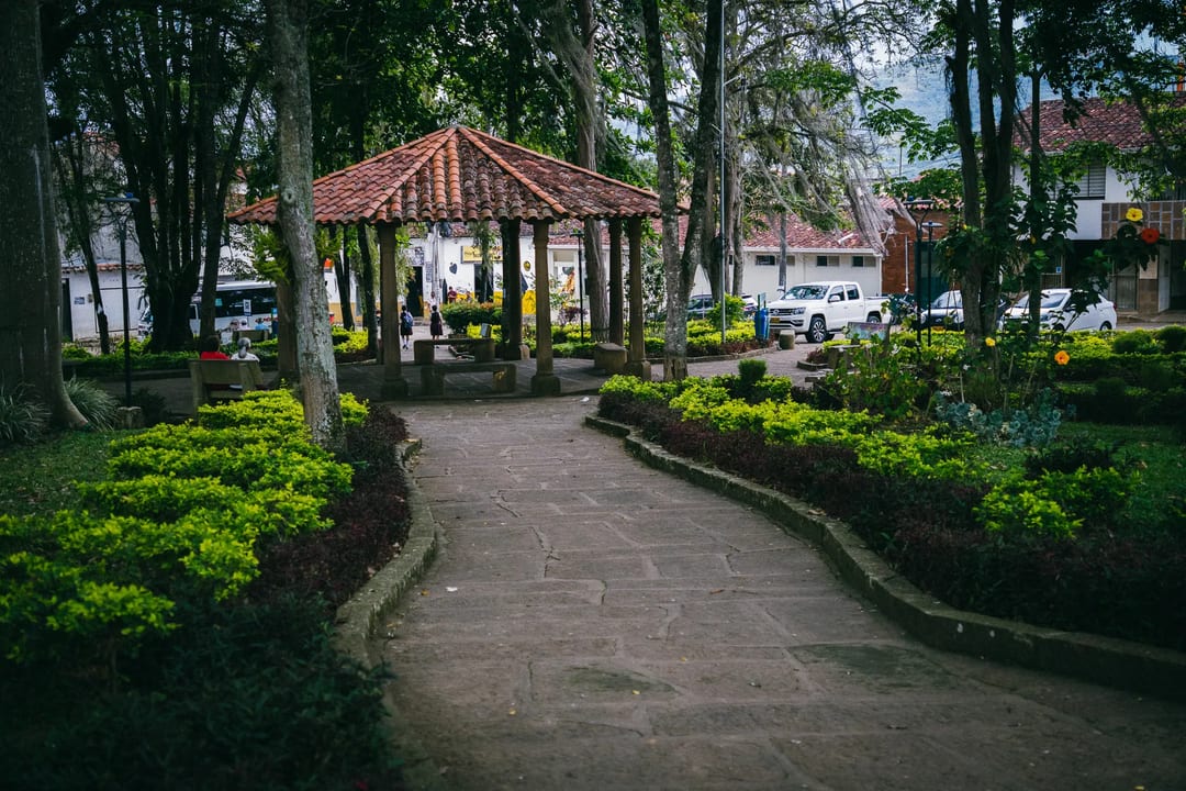 Park path leading to gazebo in El Páramo, Colombia. Lush green foliage and trees surround the walkway.