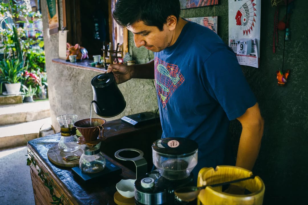 Man pouring coffee using pour-over method in cafe setting.