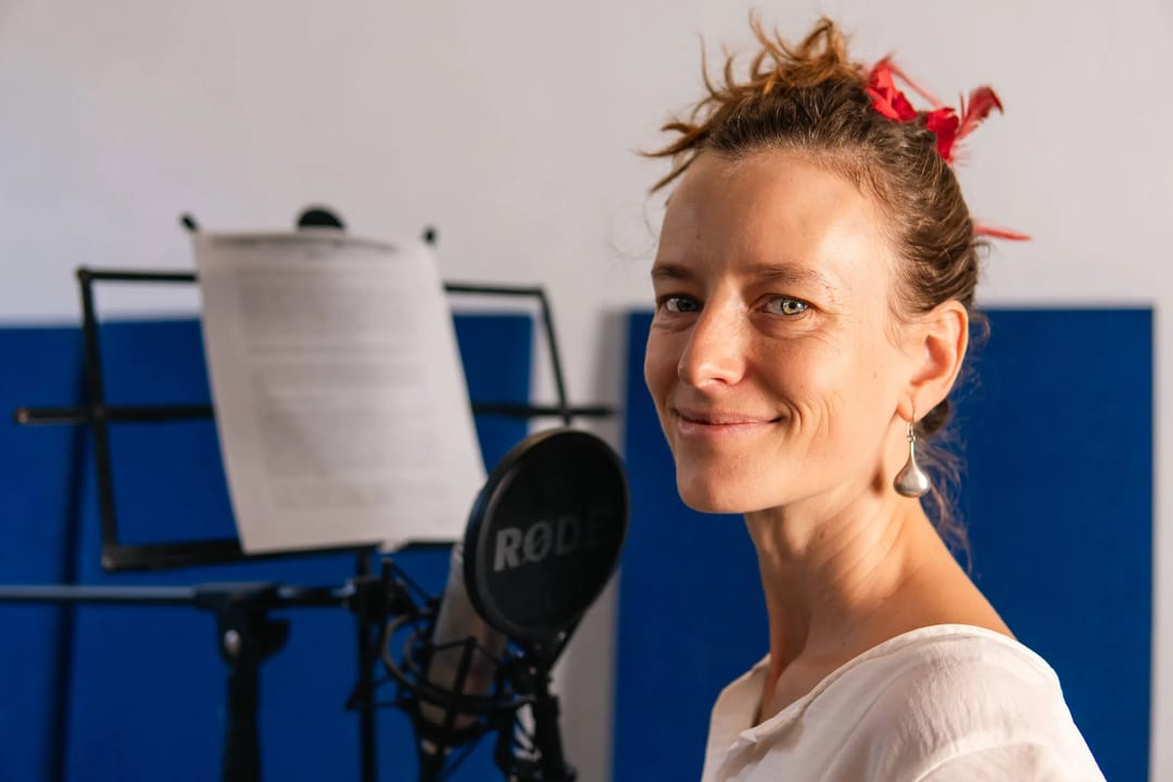 Woman recording voiceover at microphone with script. Studio setting.
