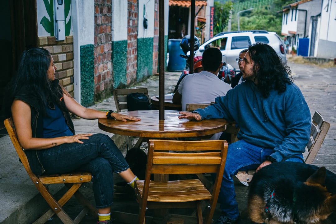 People chatting at outdoor cafe table with dog nearby. Relaxed, casual setting.