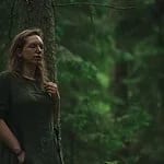 A woman in a green dress leaning against a tree with her eyes closed, during a forest bathing walk.
