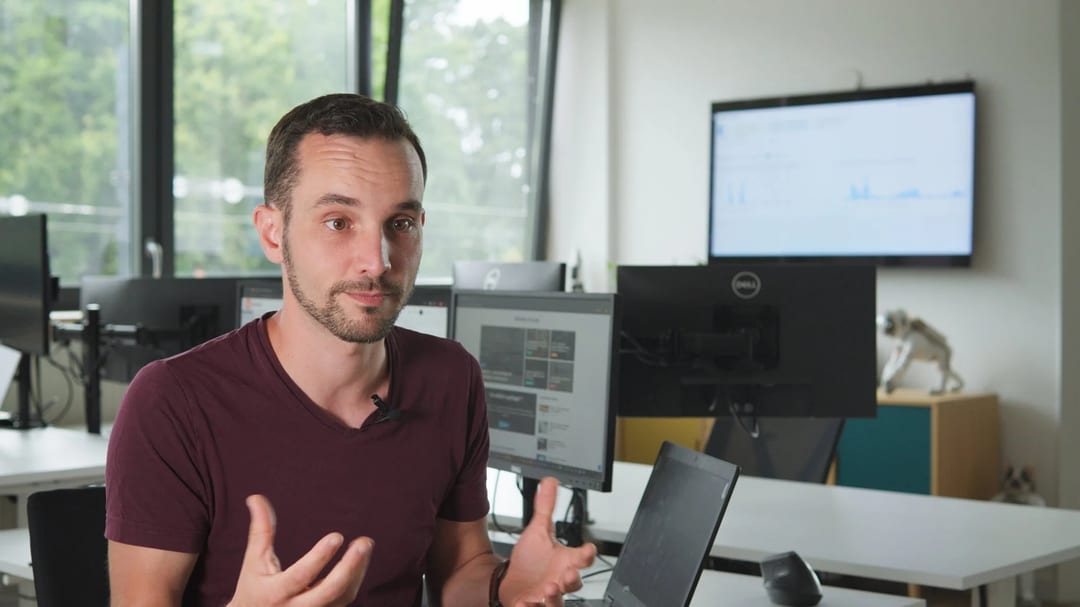 Man in office setting with multiple monitors displaying data, likely discussing Sindup analytics.