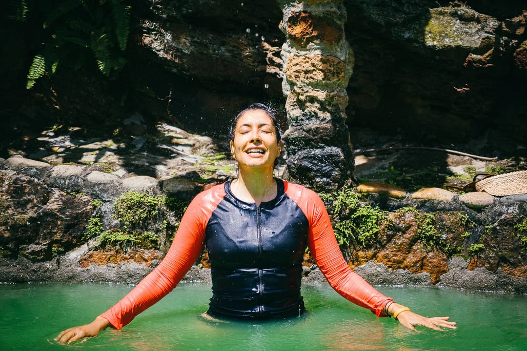 Woman enjoying a refreshing swim in a natural pool surrounded by lush greenery.